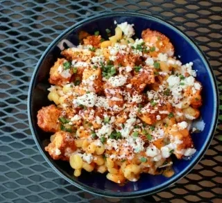 Bowl of buffalo chicken mac and cheese with crumbled cheese and herbs.