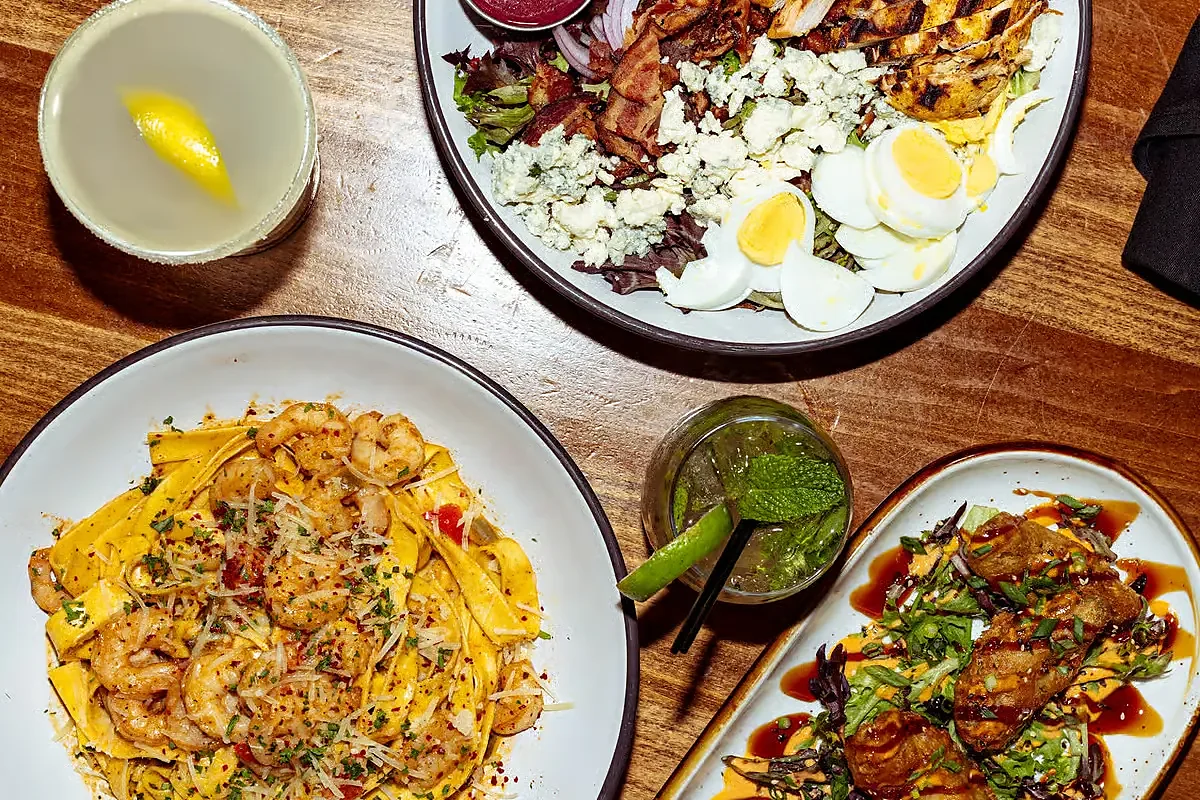 Overhead view of shrimp pasta, cobb salad, appetizer and cocktail
