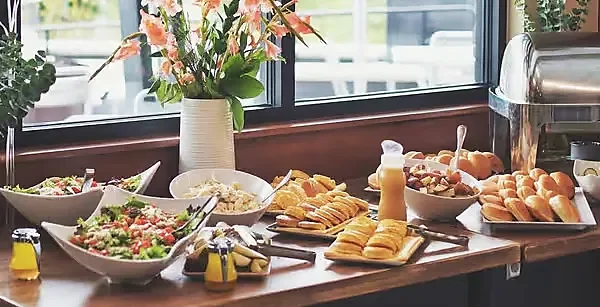 Buffet spread of salads, pastries and rolls beside a window