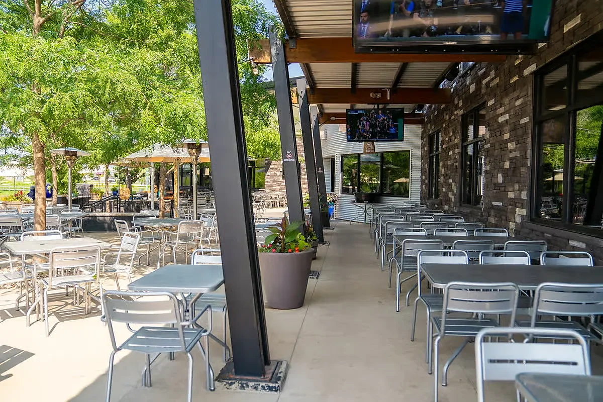 Covered outdoor patio with metal tables, televisions and shade trees