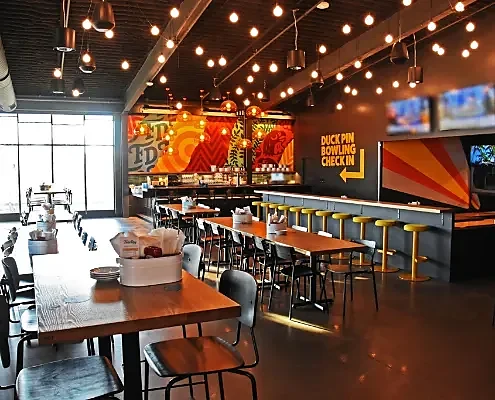 Taproom interior with communal tables, bar seating and duckpin bowling signage