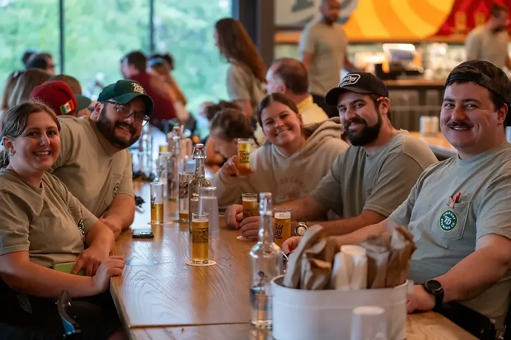 Group seated at long wooden bar table with glasses of beer