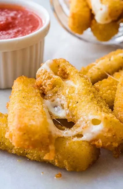 Golden-brown fried mozzarella sticks, one broken with gooey cheese, and marinara sauce.
