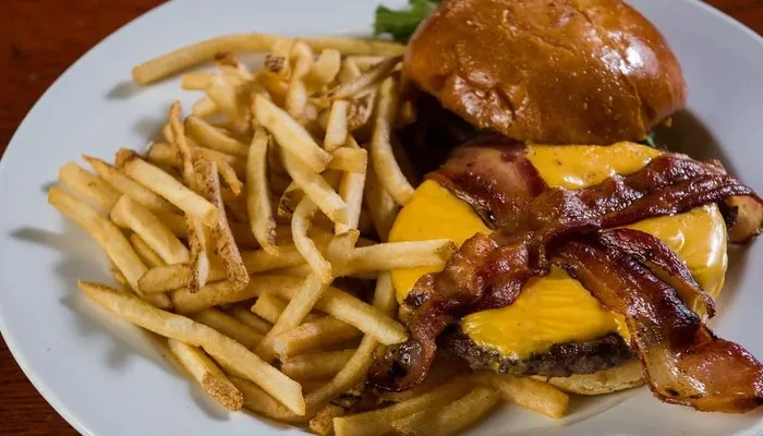 Close-up: Cheeseburger with bacon, melted cheese, and golden fries.