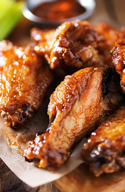 Detailed shot of charred, glazed chicken wings on parchment with sauce.