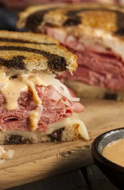 Close-up of a cut Reuben sandwich on marbled rye with dressing.