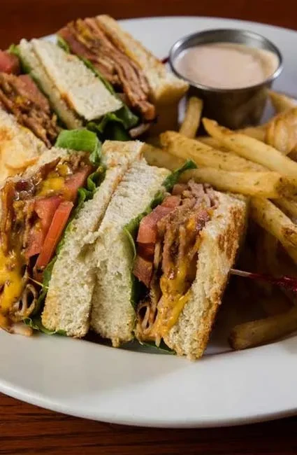 Club sandwich, cut into triangles, with french fries and dipping sauce.