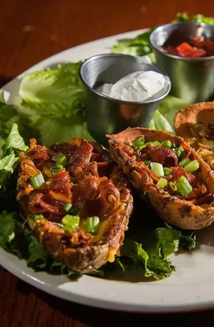 Plate of loaded potato skins with cheese, bacon, sour cream, and salsa.