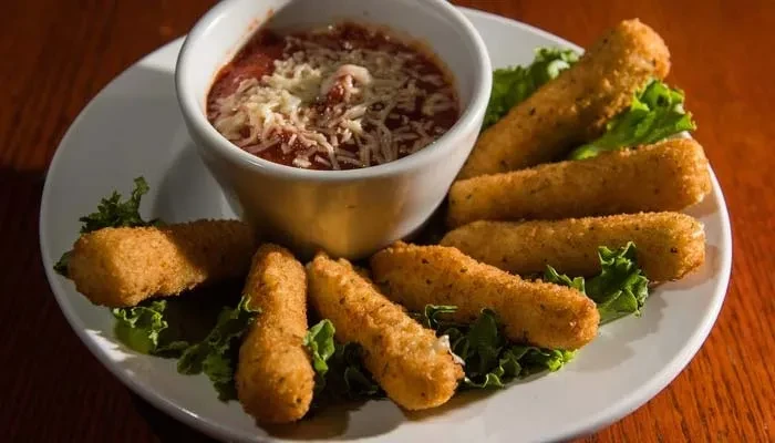 Golden-brown mozzarella sticks, marinara sauce topped with shredded cheese.