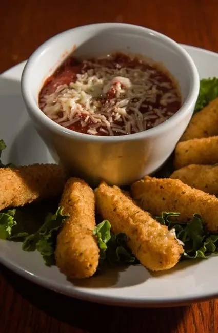 Marinara sauce with cheese, surrounded by golden mozzarella sticks and lettuce.