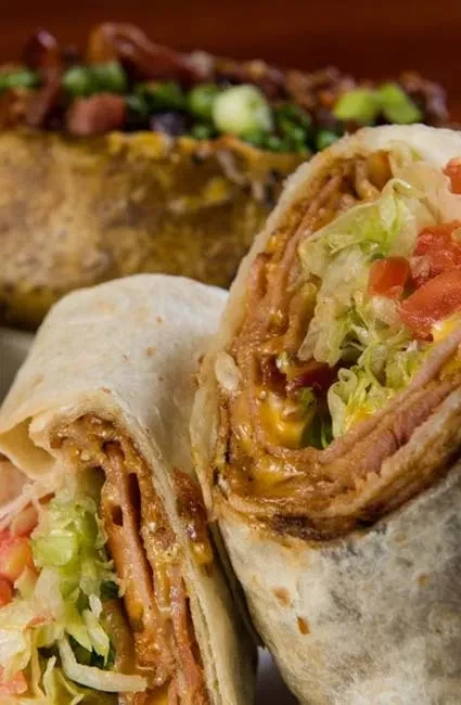 Close-up of a halved wrap with meat, cheese, lettuce, and tomatoes.