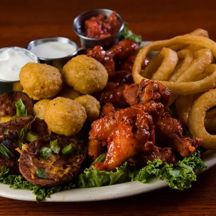 Assorted platter of buffalo wings, onion rings, potato skins, and fried appetizers.