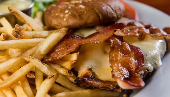 Plate with french fries and a bacon cheeseburger with lettuce and tomato.