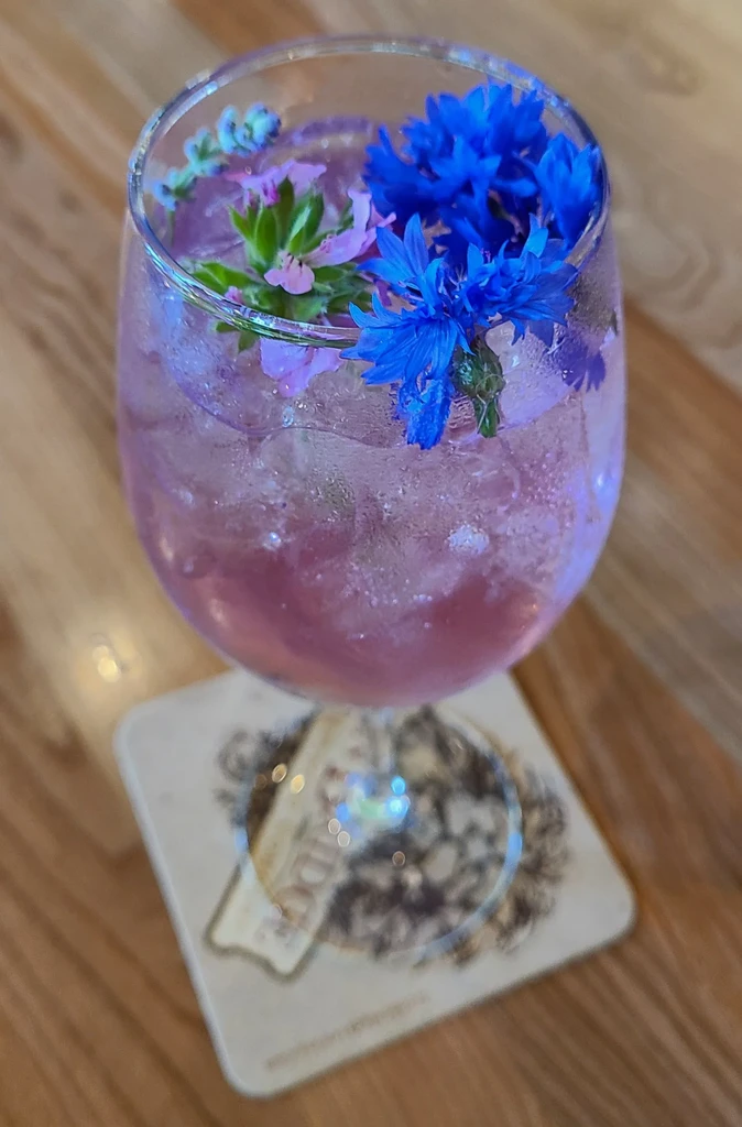 Purple drink with ice and blue flowers in a stemmed glass.