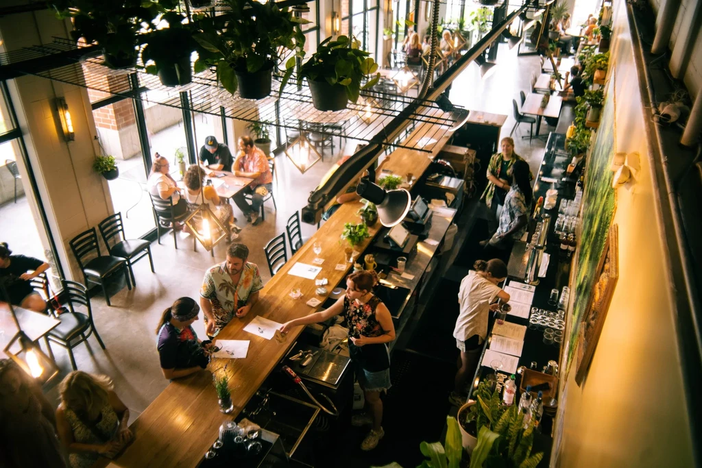 Busy industrial-chic restaurant interior with patrons at bar and tables.