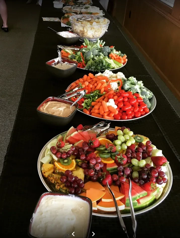 Buffet table featuring fresh cut fruits, raw vegetables, and dips.