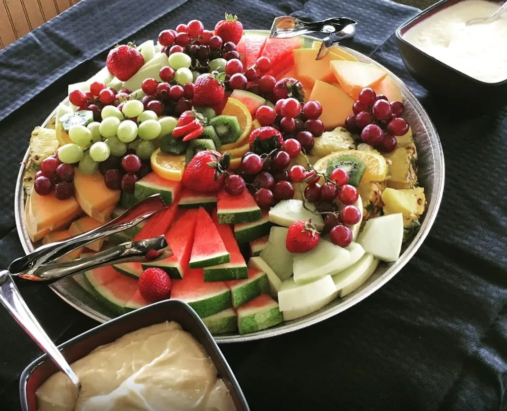 Large silver platter with fresh, colorful cut fruits and serving tongs.