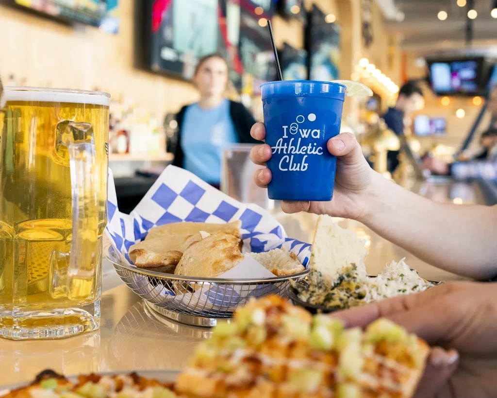 Sports bar table with beer, food, and 'Iowa Athletic Club' cup.