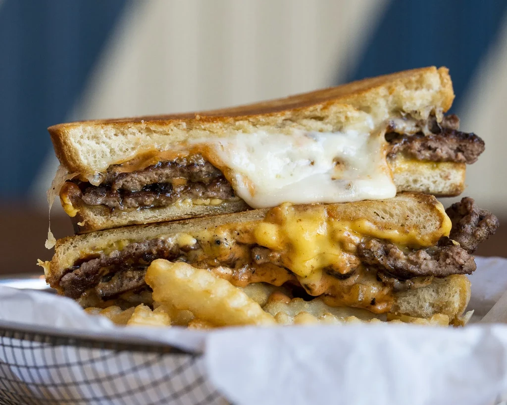 Close-up of a double patty melt with oozing cheese and crinkle-cut fries.
