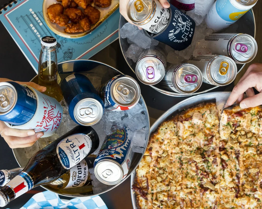 Overhead shot of hands with pizza, wings, drinks at sports restaurant.