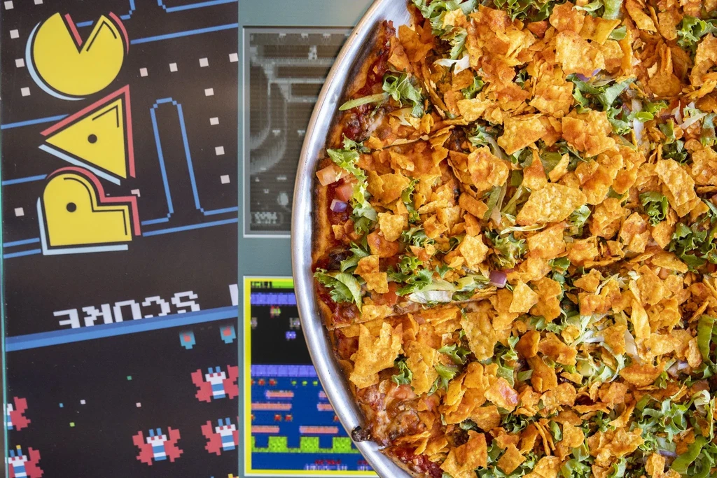 Pizza topped with crisps and lettuce against a retro arcade background.