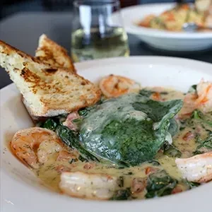 Bowl of shrimp, spinach, and creamy sauce, with toasted bread.