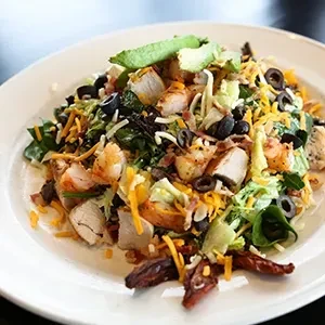 Large colorful chicken salad with avocado, bacon, cheese, and olives.