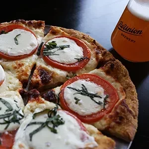 Close-up of sliced Margherita pizza and a glass of ReUnion beer.