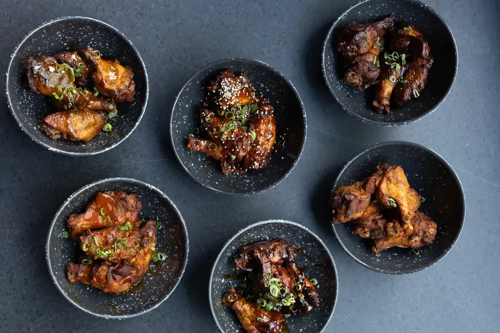 Six individual servings of varied chicken wings in dark bowls.