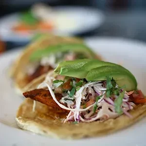 Three tacos with fried fish or chicken, coleslaw, avocado, cilantro.