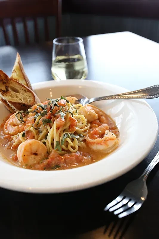 Close-up: Shrimp pasta with herbs, tomatoes, baguette, and wine.