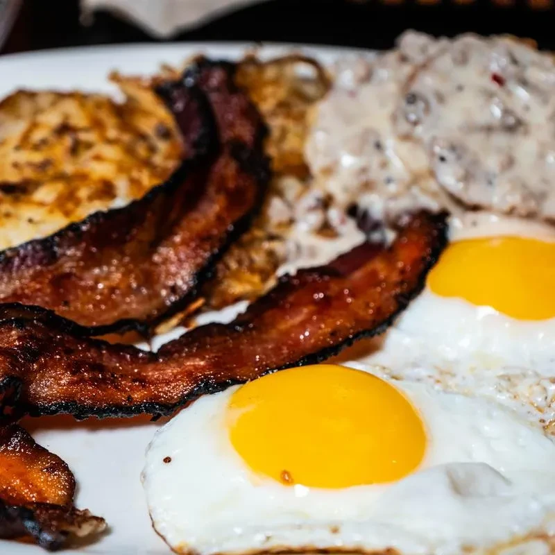 Close-up of a breakfast plate with crispy bacon, fried eggs, and hash browns.