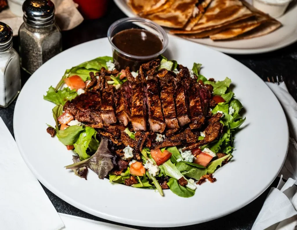 Sliced medium-rare steak salad with blue cheese, tomatoes, and dressing.