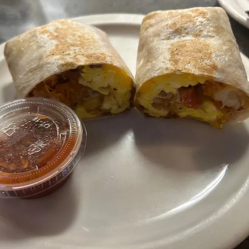 Two breakfast burritos, one cut open, revealing eggs, potatoes, and salsa.