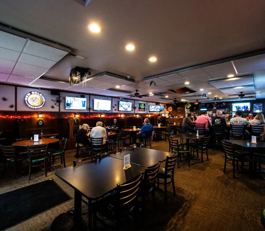 Dim, casual pub interior with patrons, bar, TVs, and Halloween decor.