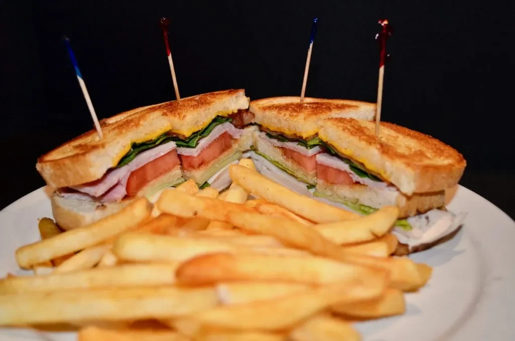 Club sandwich cut in half, served with fries and a pickle.