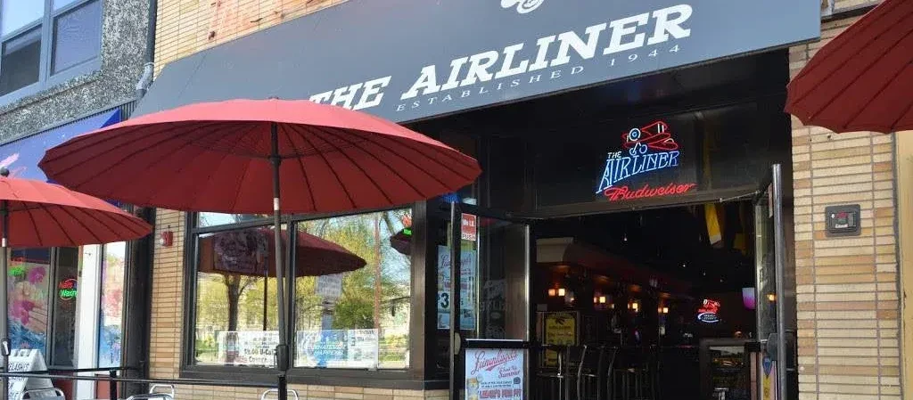 THE AIRLINER storefront with awning, patio umbrellas, and bright neon sign.