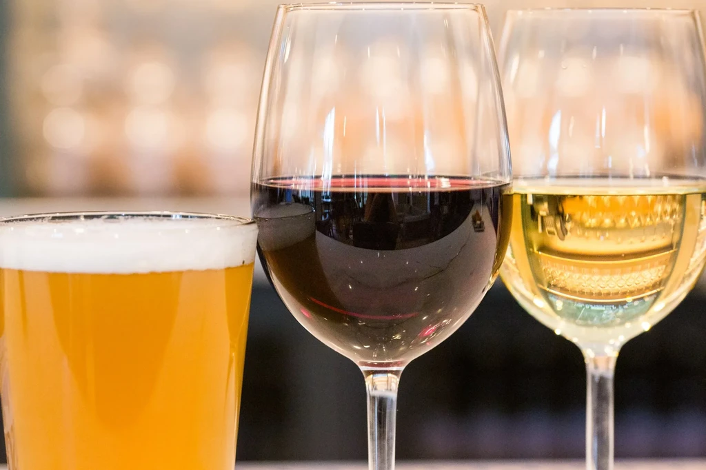 Beer, red wine, white wine glasses against blurred background.