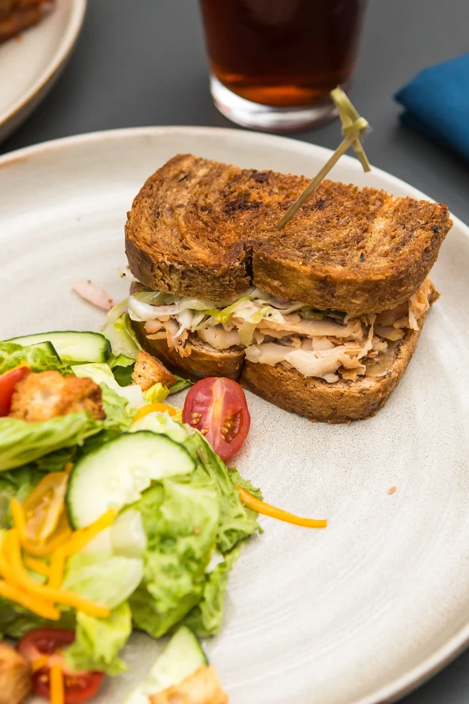 Grilled deli sandwich, fresh side salad, and dark beverage on a plate.