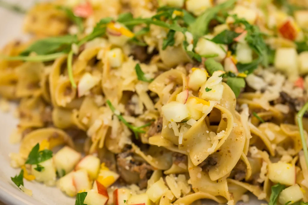 Close-up of broad pasta with ground meat, diced apples, and fresh herbs.