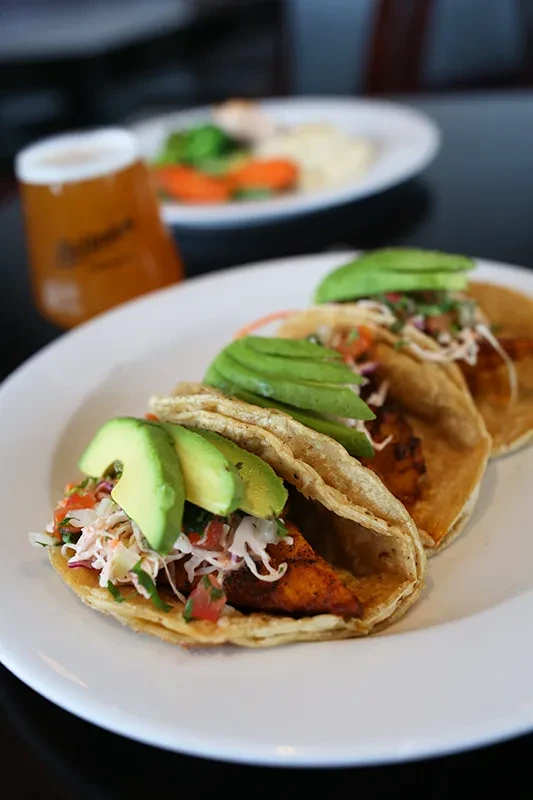 Three tacos filled with protein, coleslaw, pico de gallo, and avocado.