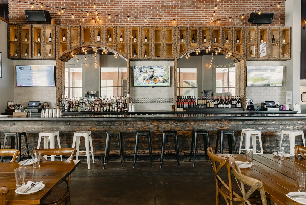 Restaurant bar interior: brick wall, TVs, bottles, and bar stools.