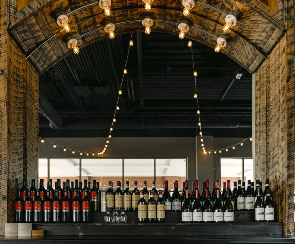 Warm-lit rustic archway and shelves filled with red wine bottles.