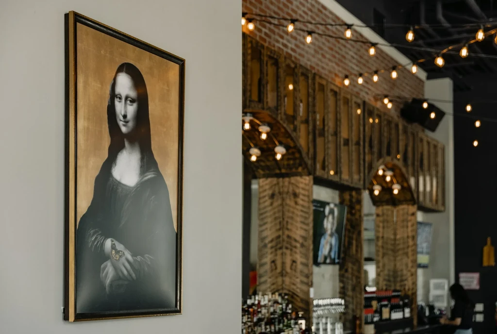 Grayscale Mona Lisa art with butterfly, beside blurred rustic bar.