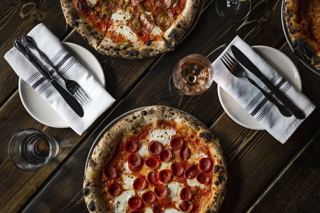Rustic table with pepperoni and jalapeño pizzas, drinks, and settings.