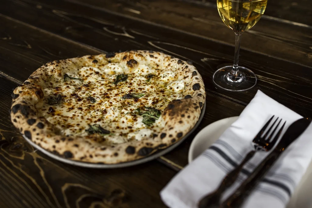 Neapolitan pizza, white wine, and place setting on a dark wooden table.