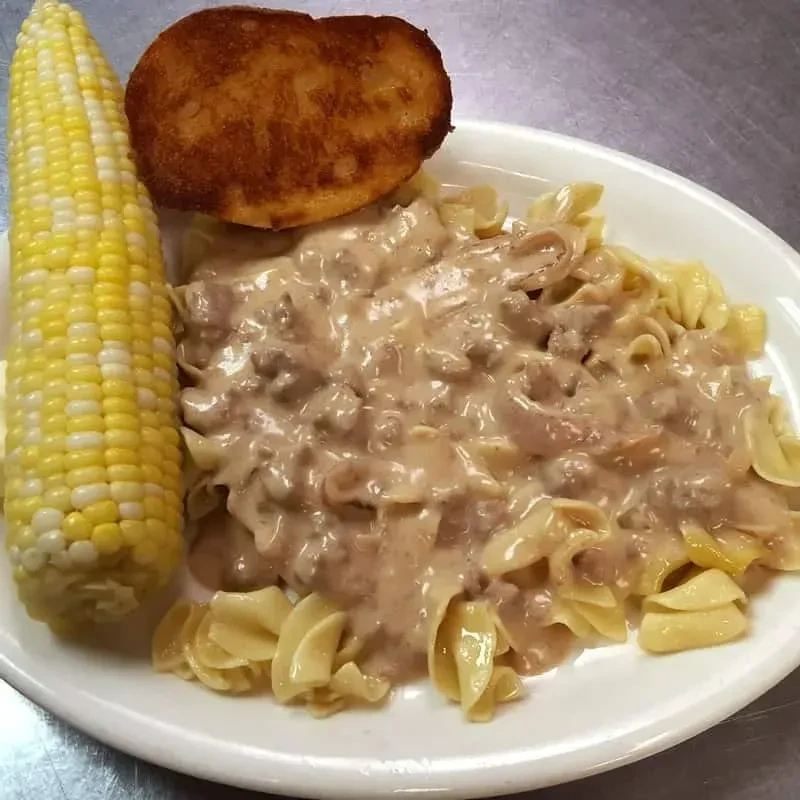 Creamy pasta with ground meat, corn, fried patty on plate.