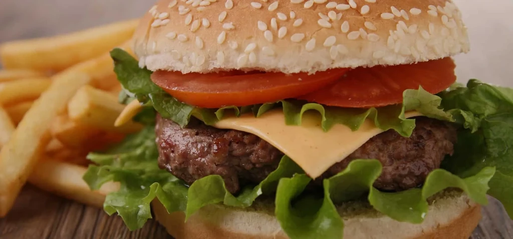Close-up cheeseburger with beef patty, melted cheese, lettuce, tomato, fries.