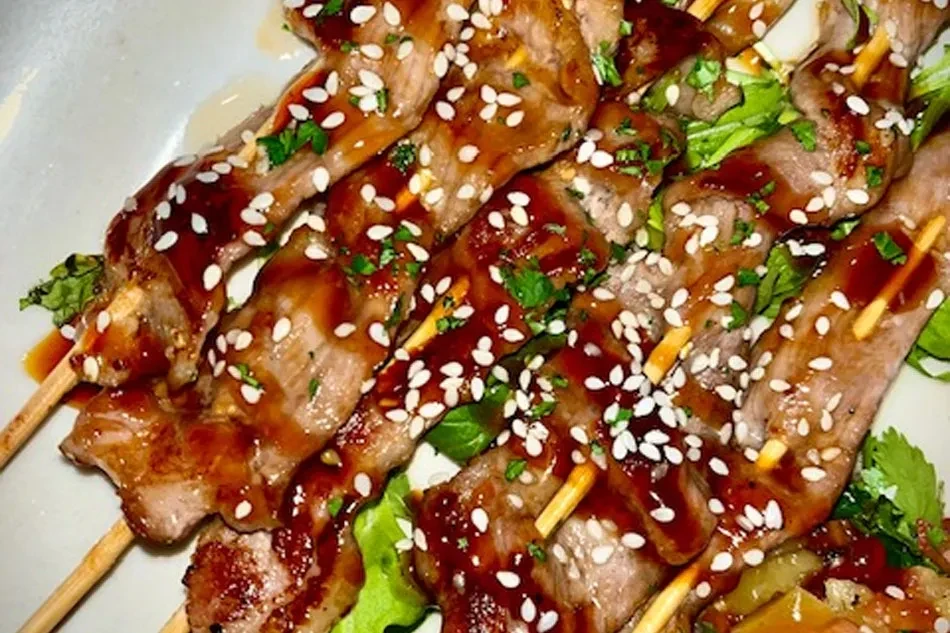 Close-up of glazed meat skewers with sesame seeds and green herbs.