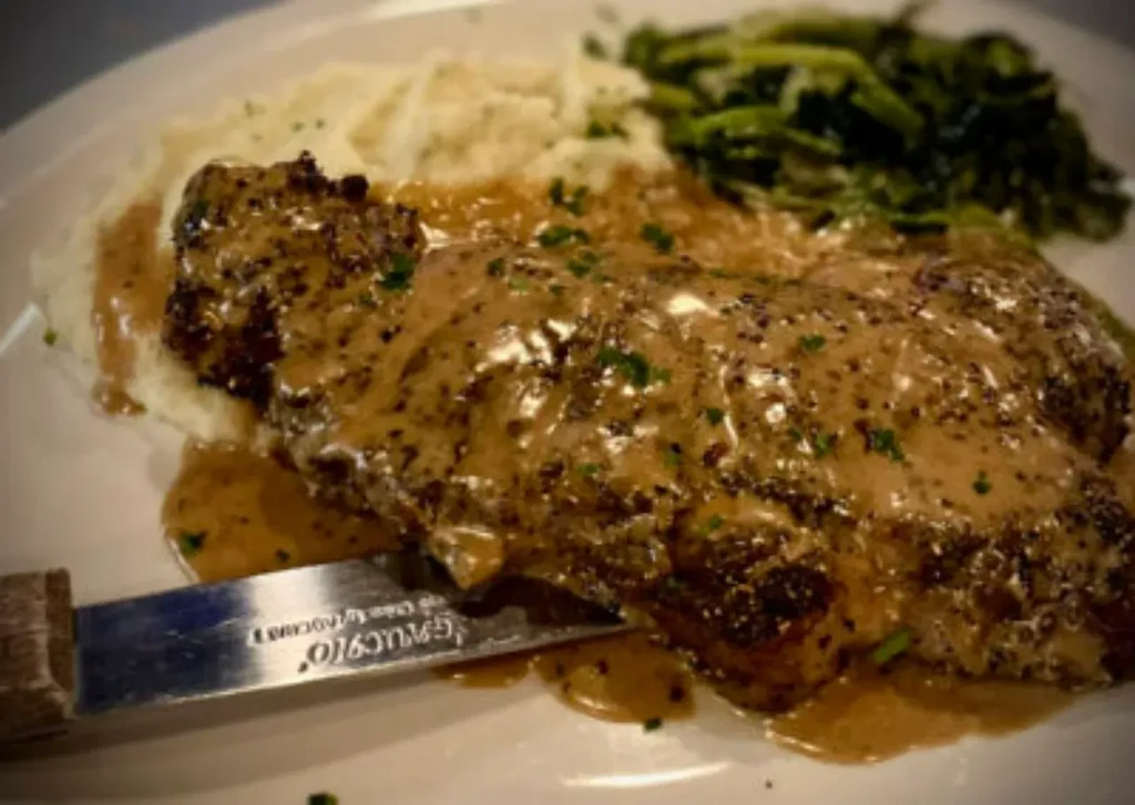 Large meat with gravy, mashed potatoes, and leafy greens.